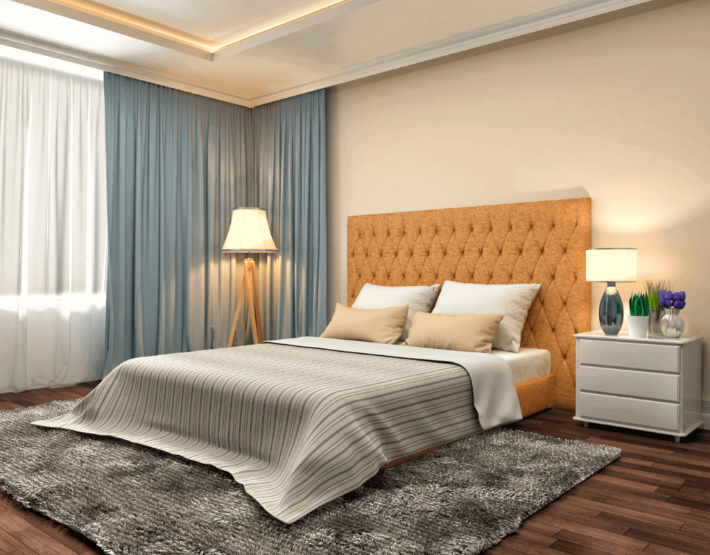 Gezellige slaapkamer met een mosterdkleurig getuft hoofdeinde, grijs beddengoed, een vloerkleed met structuur en lichtblauwe gordijnen.