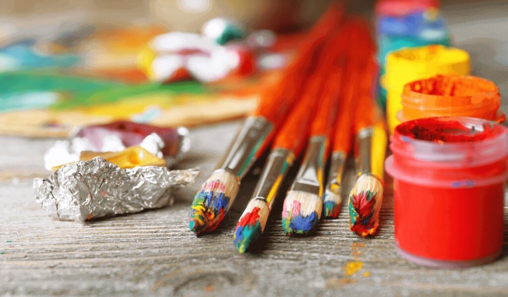 Paint brushes and jars on a wooden surface with colorful splashes.