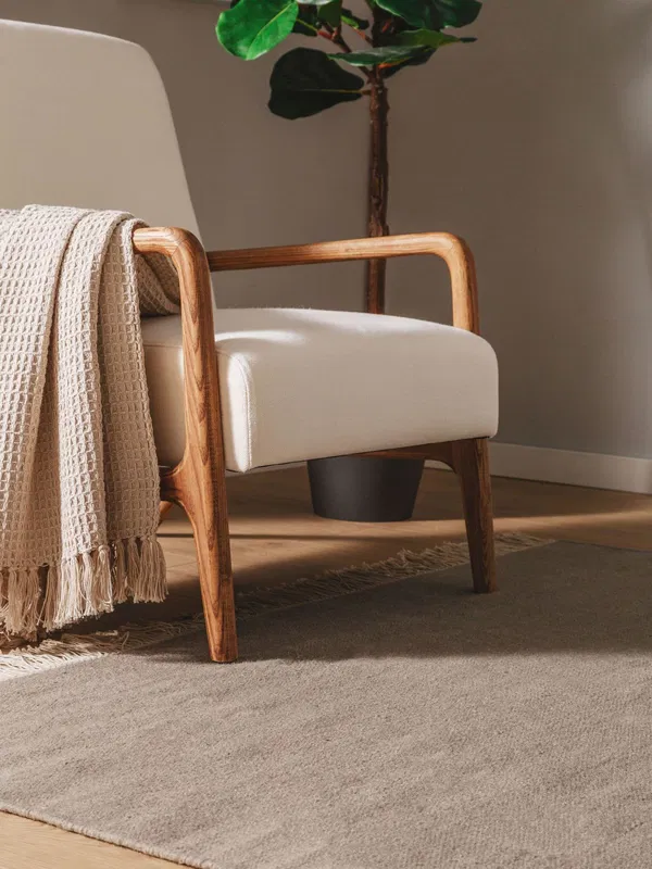 Beige armchair with wooden armrests and a woven blanket on a light grey rug in a modern living room. Let me know if you'd like further changes!